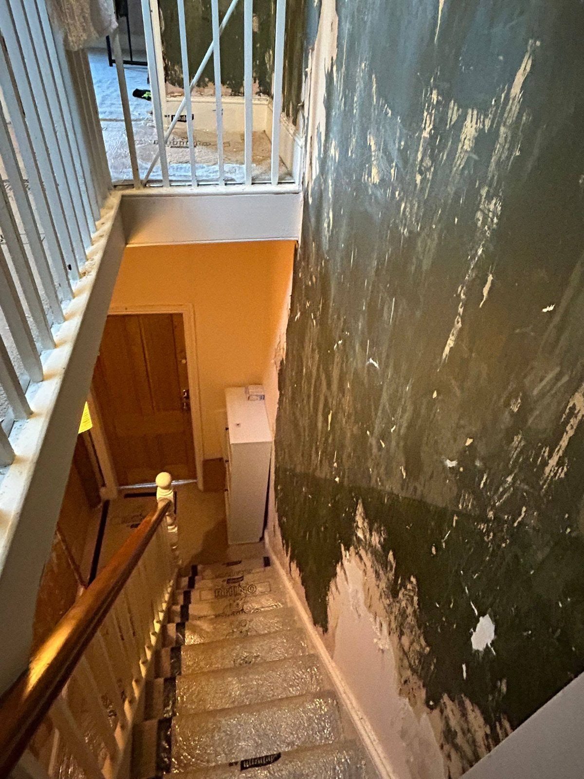 Stairwell before: walls half stripped of old paper and paint, plaster blown