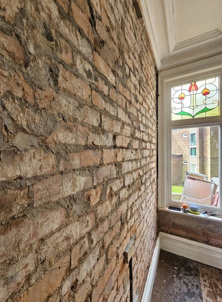 Bare brick wall beside a window with a stained glass top light