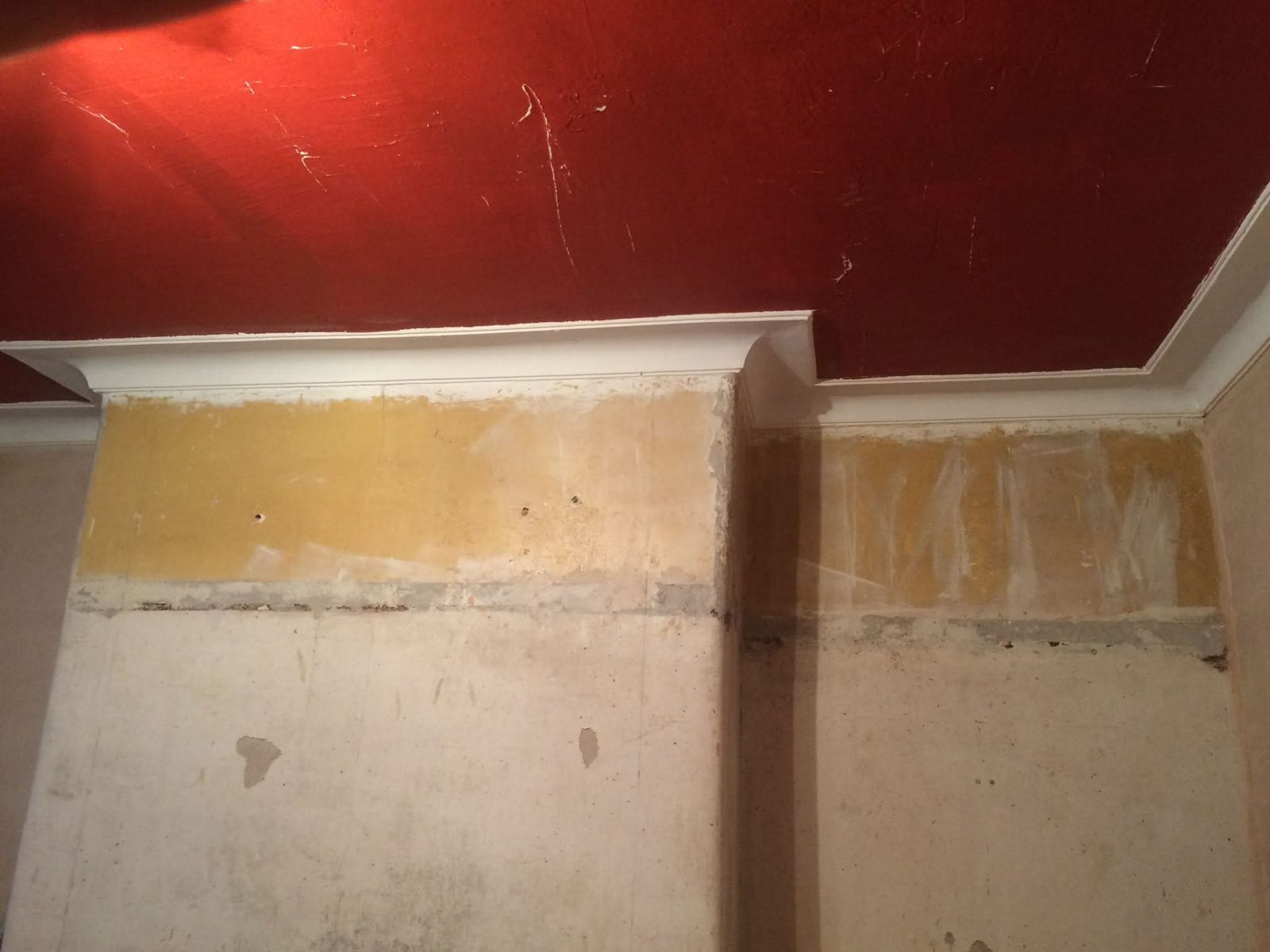 Wall stripped back below a cornice with a red painted ceiling above