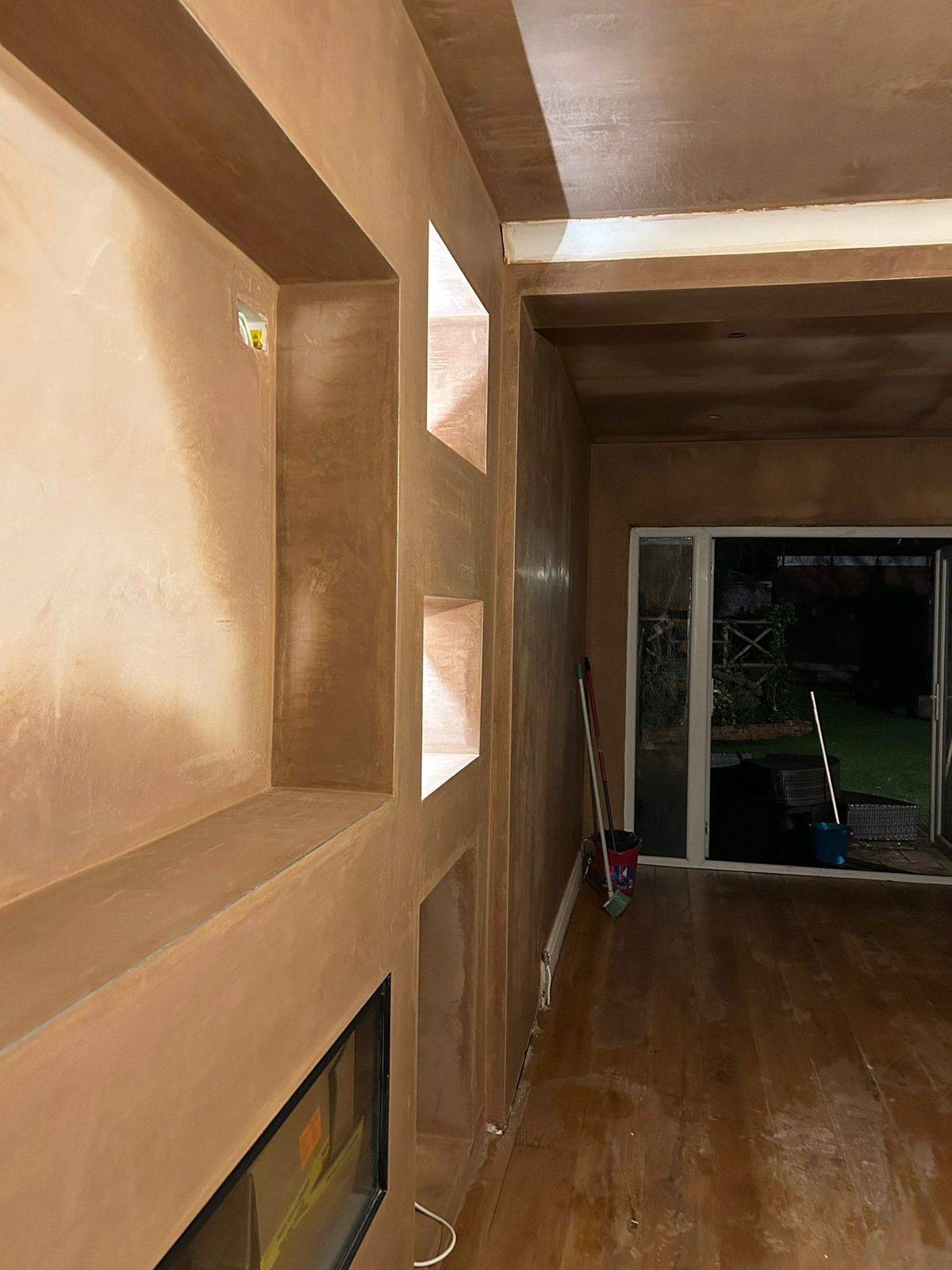 Freshly plastered media wall with recessed shelves and a fireplace opening