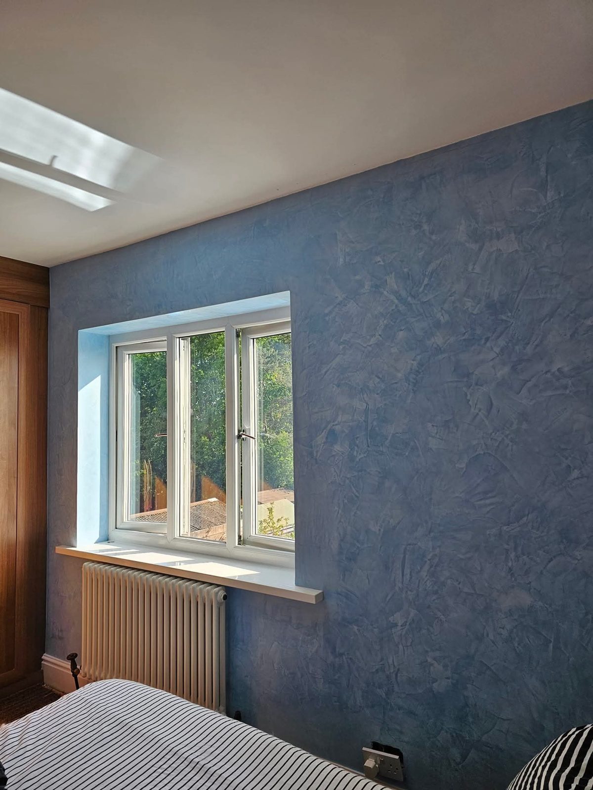 Bedroom with a blue polished plaster wall around a sash window