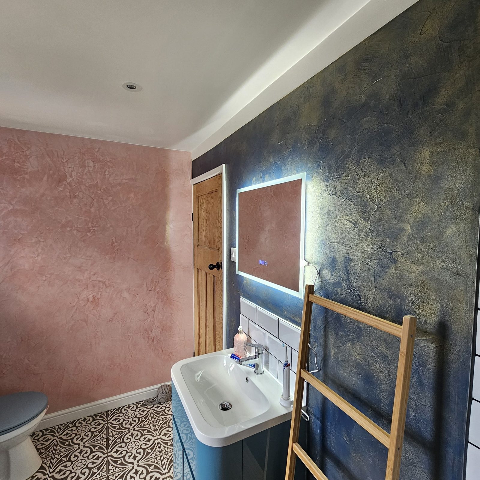 Bathroom with a dark navy and gold textured feature wall beside blush pink plastered walls